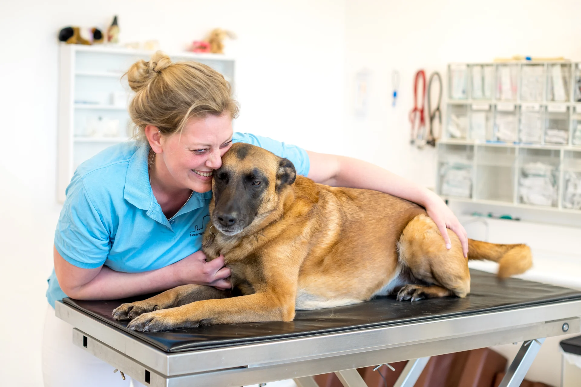 Hund auf Behandlungstisch mit Tierärztin die mit ihm kuschelt
